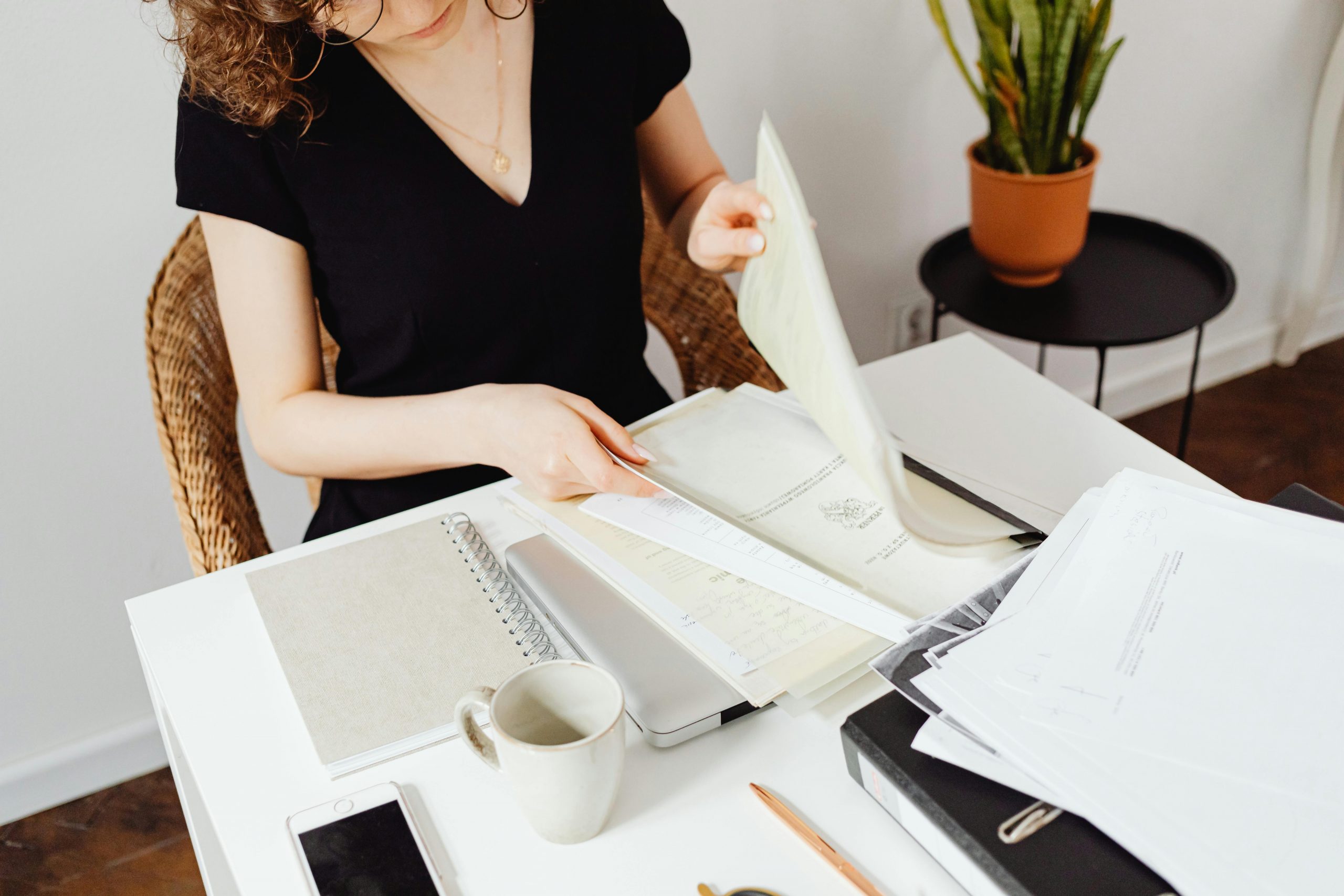 Woman sorting through documents in a home office setting. Organized workspace with plants.